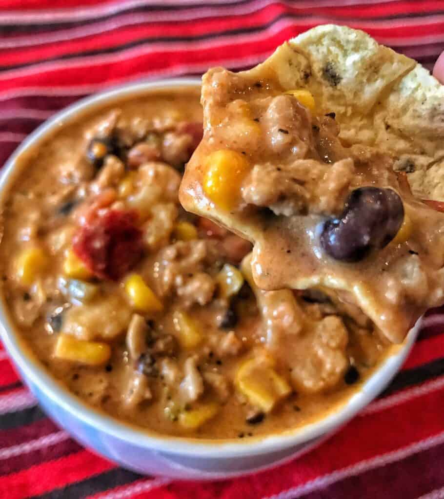 creamy taco high protein soup in a bowl with a baked tortilla chip dipped in it