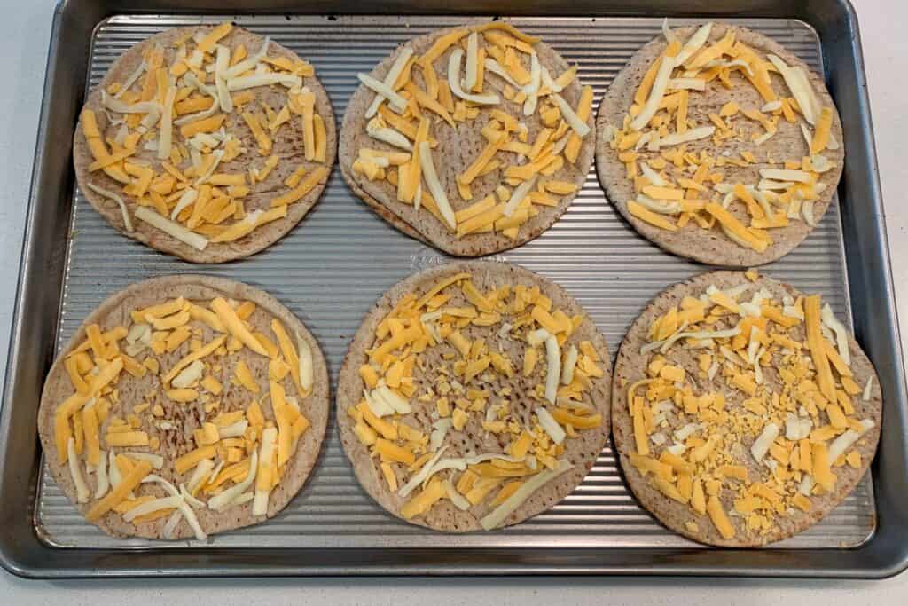 pitas on a baking sheet with shredded cheese