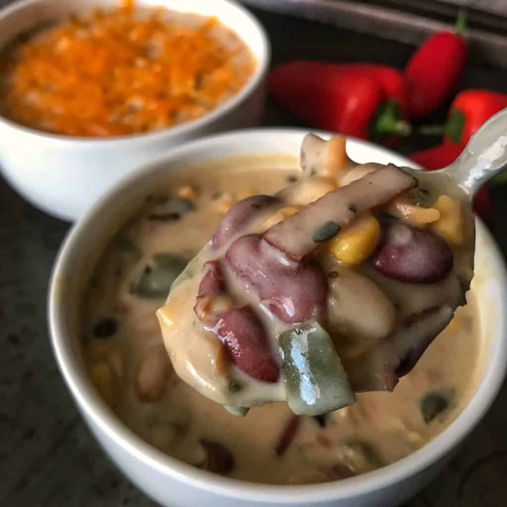 bean and bacon soup on a spoon with a bowl topped with cheddar cheese in the background
