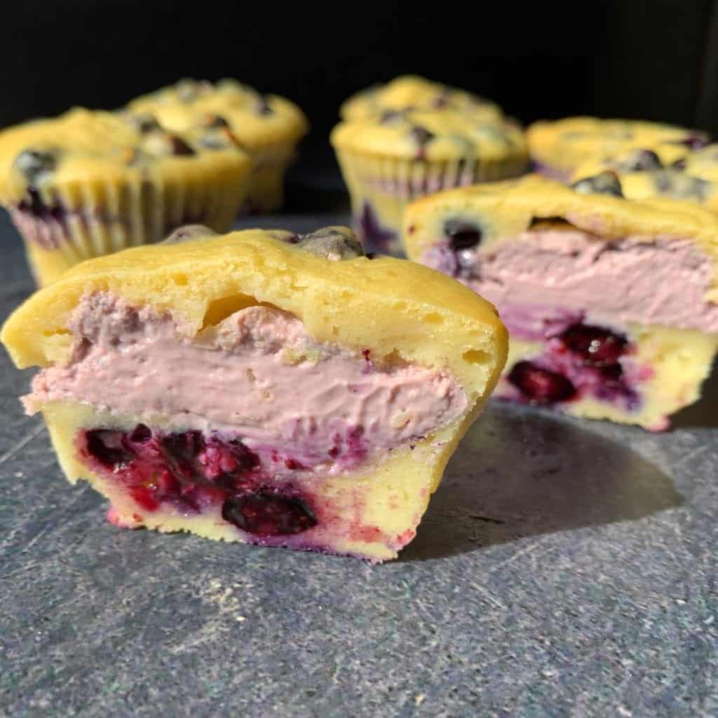 a blueberry cheesecake muffin cut in half to show a layer of cheesecake inside