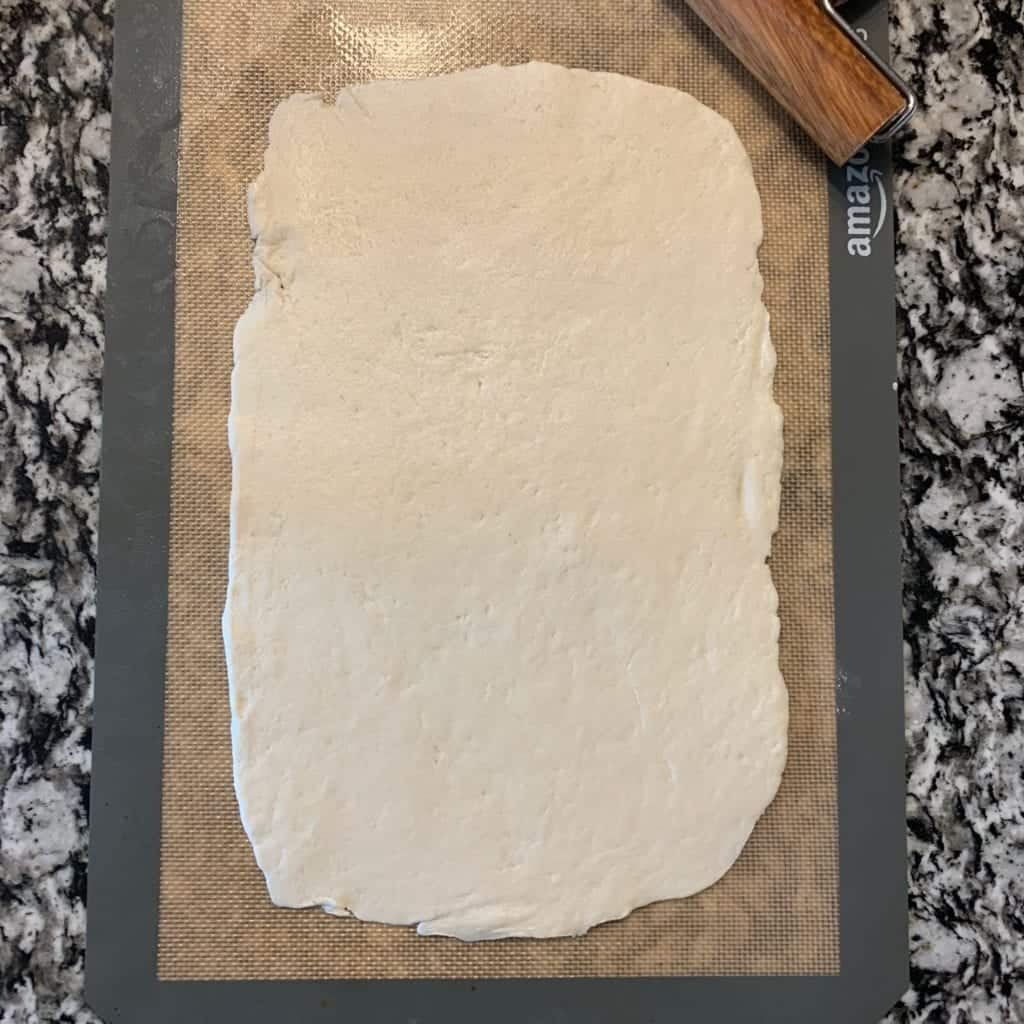 pizza crust dough rolled out on a baking mat