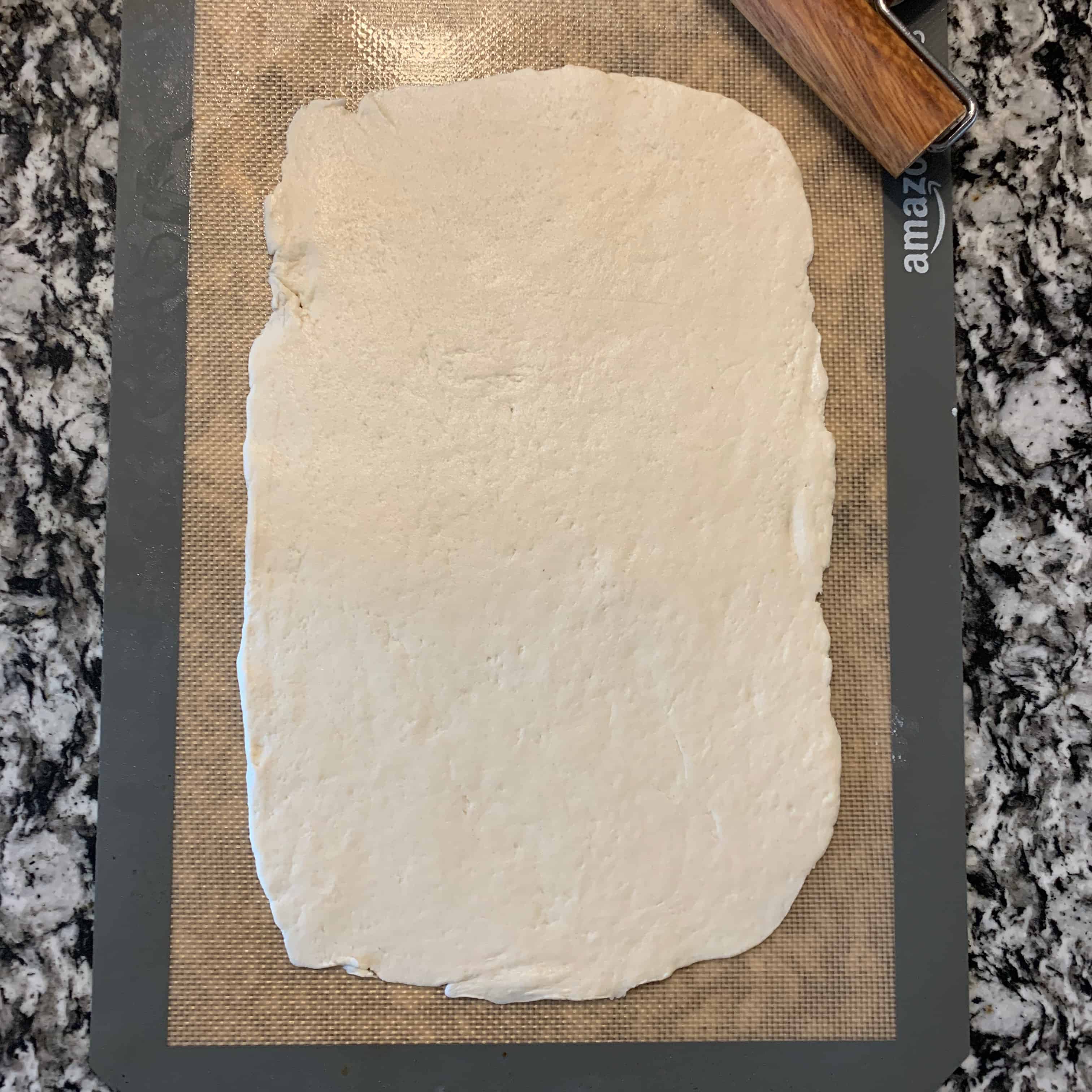 pizza crust dough rolled out on a baking mat