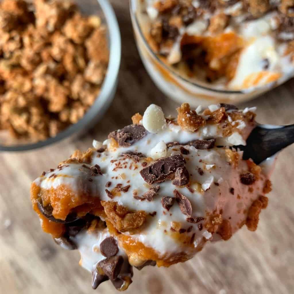 a spoon with pumpkin spice protein parfait overlooking a bowl of protein granola