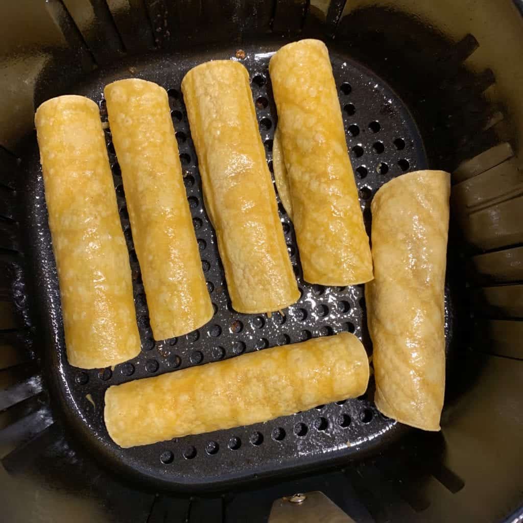 6 bean and cheese taquitos in an air fryer basket before cooking