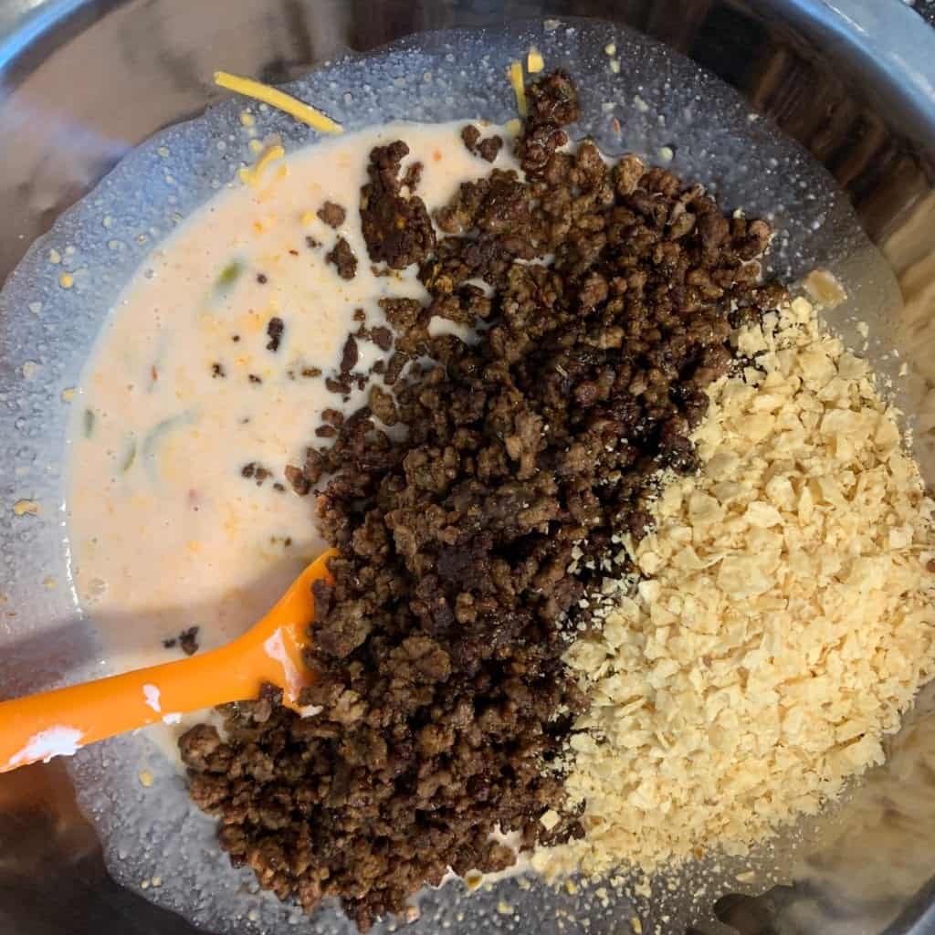 liquid taco bites ingredients mixed together in a bowl with the ground beef and crushed tortilla chips on top