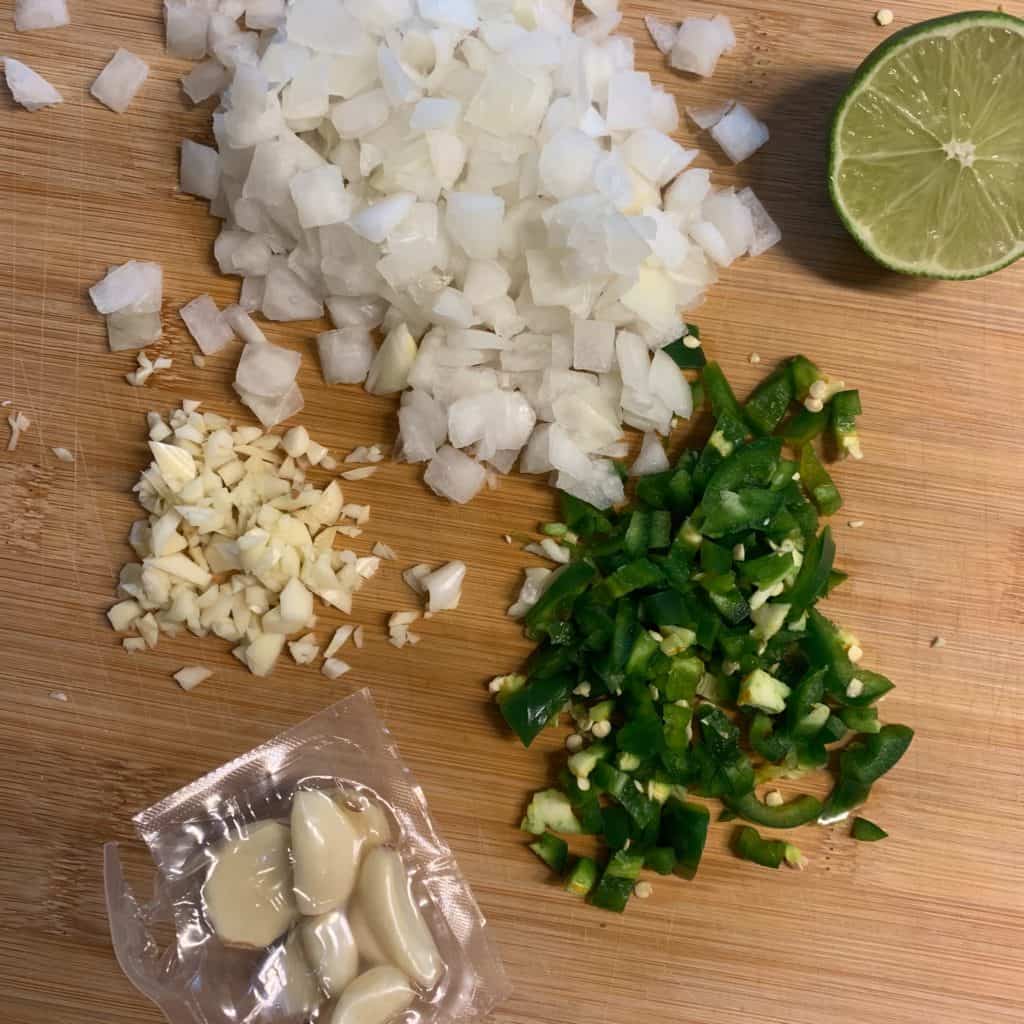 onion, jalapeño, and garlic on a cutting board with half a lime