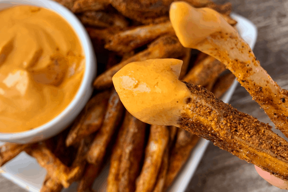 two nacho fries dipped in cheese sauce over a plate of fries