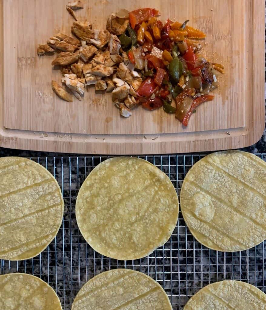 cooked and chopped fajita chicken and peppers beside extra thin corn tortillas on a wire rack