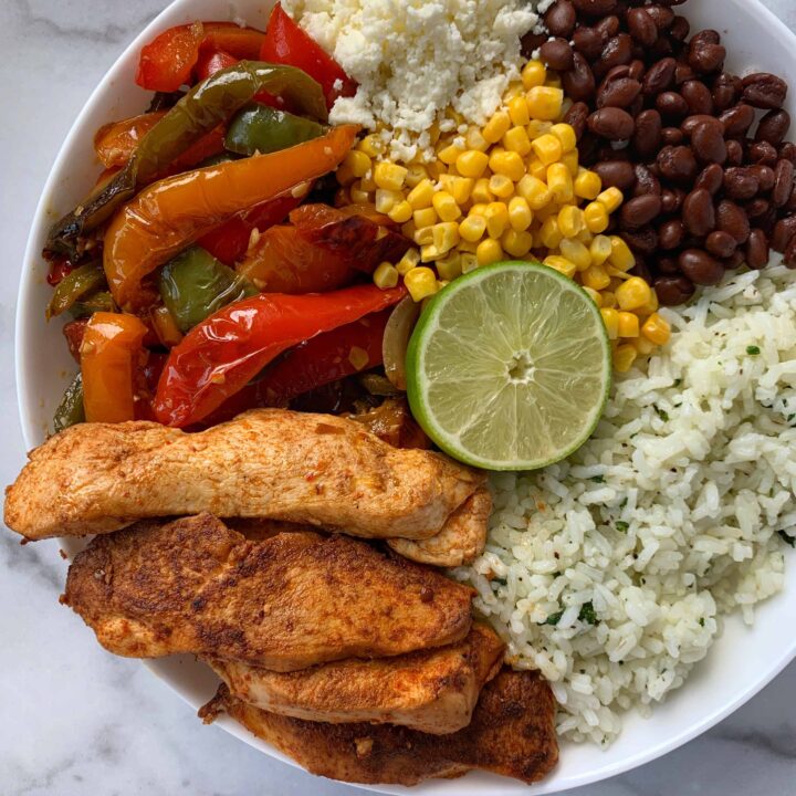 fajita chicken and peppers in a burrito bowl with cilantro lime rice, corn, black beans, cotija cheese, and half a lime