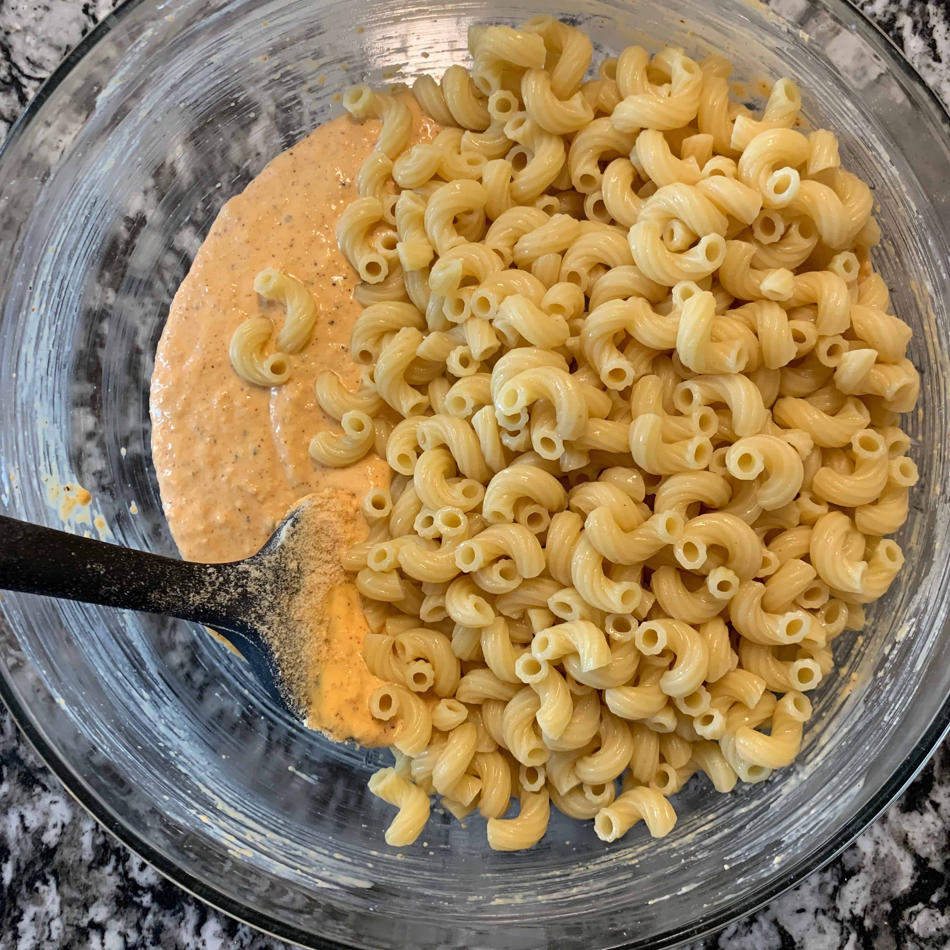 cooked pasta on top of cheese sauce in a glass mixing bowl