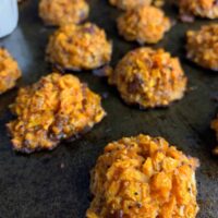 sweet potato tots on a baking sheet with a cup of honey dip in the background