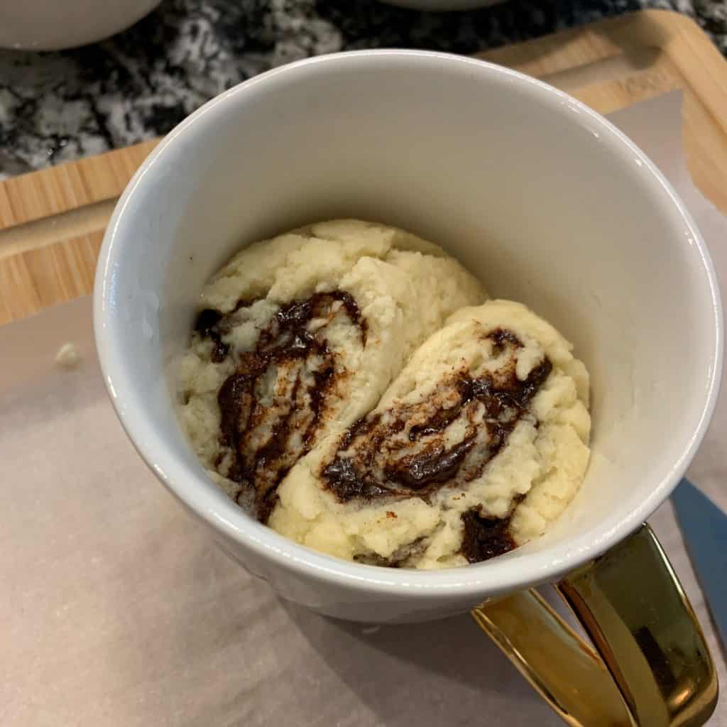 two cinnamon rolls in a mug before microwaving
