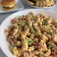 healthy pasta salad in a white bowl with burgers in the background