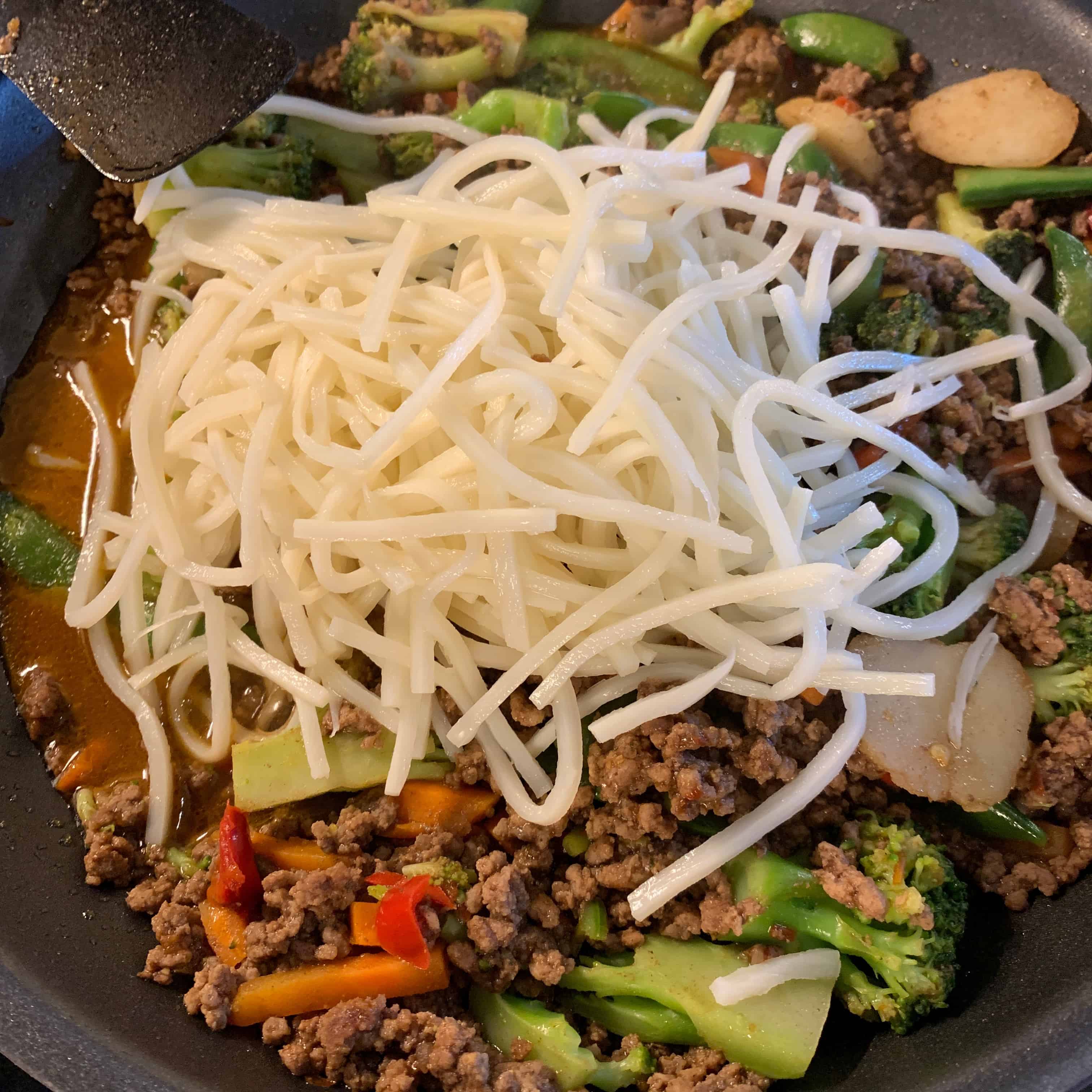 the vegetables and noodles on top of the cooked ground beef and five spice sauce