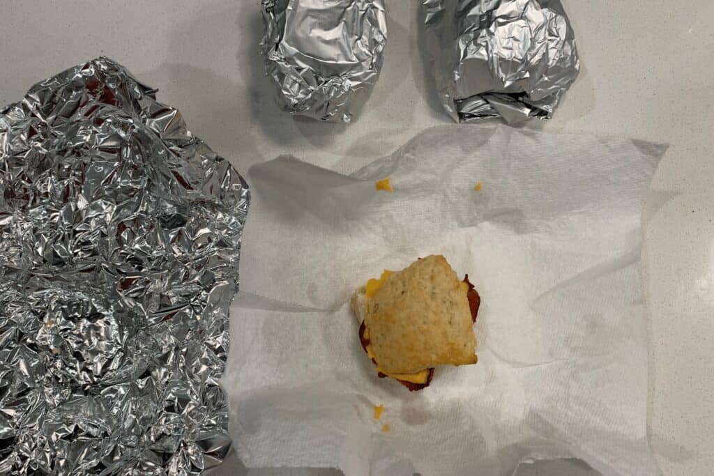 reheated biscuit on a paper towel next to other frozen biscuits wrapped in foil