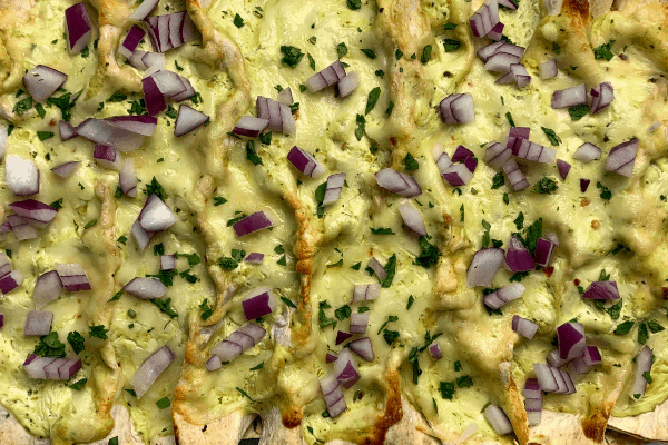 creamy chicken enchiladas in a dish with red onion and chopped cilantro on top