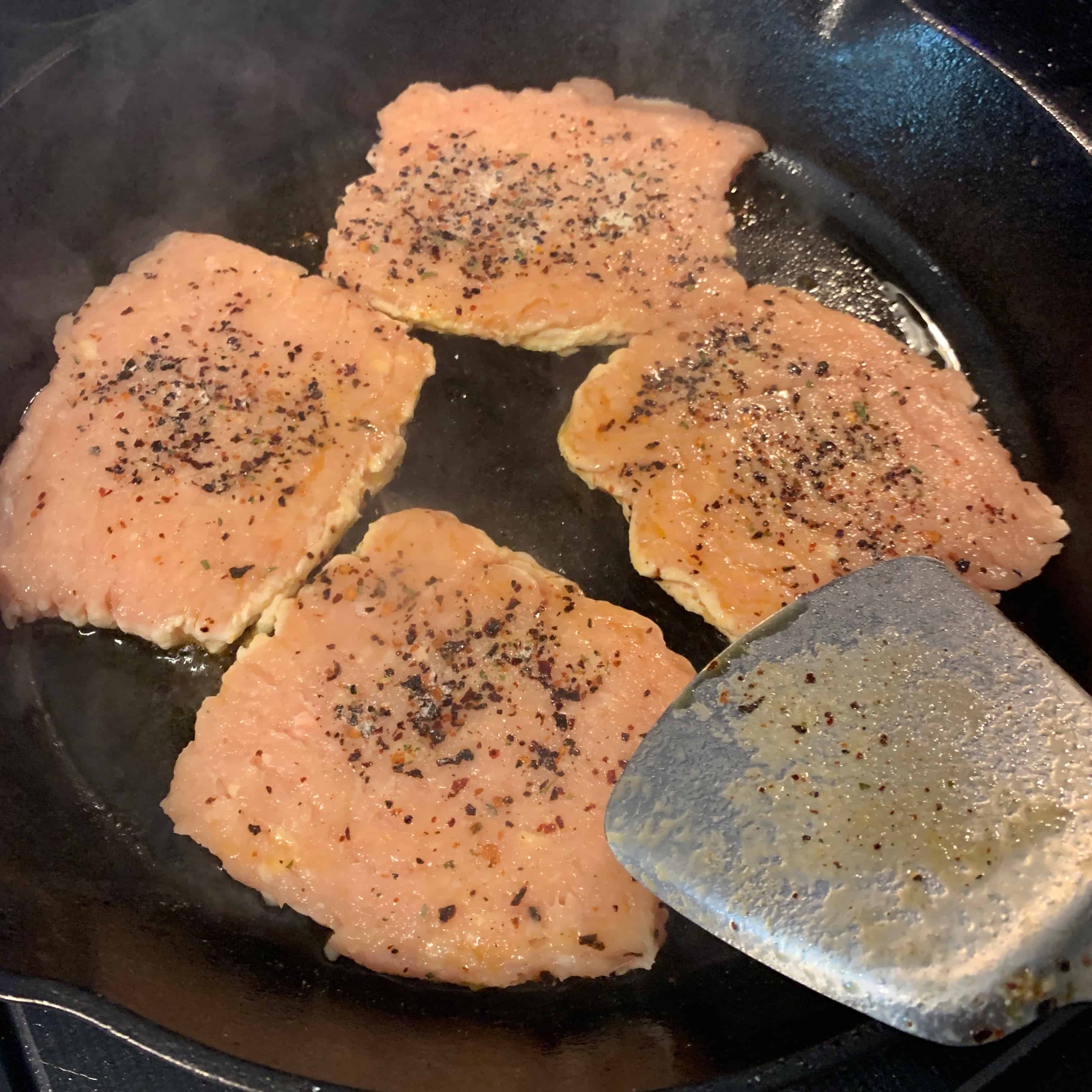 chicken burgers after pressing flat in the skillet