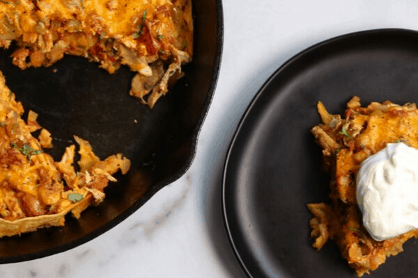 king ranch chicken casserole in a cast iron skillet with a slice on a black plate beside it