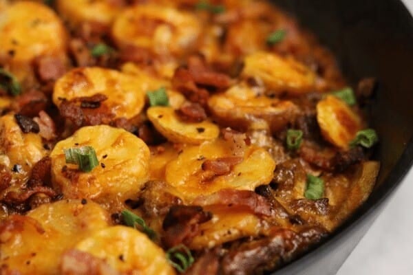 ground beef and potatoes with melted cheddar, green onion, and bacon bits in a cast iron skillet