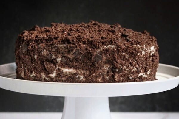 chocolate cake with cream frosting and crushed oreos on a white cake serving dish