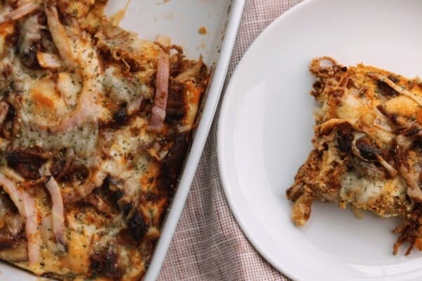pulled pork breakfast casserole in a baking dish with a piece cut out on a white plate beside it