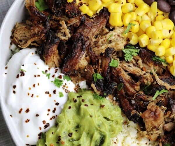 pressure cooker pork tenderloin carnitas in a bowl with corn, black beans, Greek yogurt, guacamole, cotjia cheese, and cauliflower rice