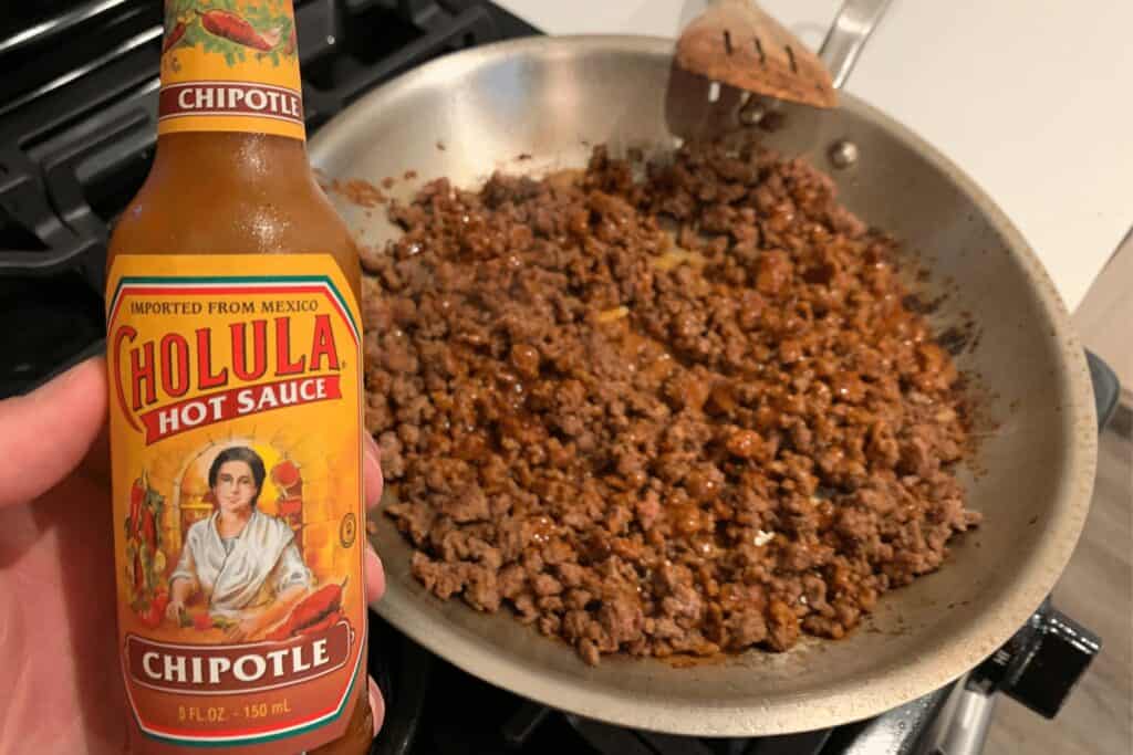 adding chipotle cholula hot sauce to the cooked ground beef