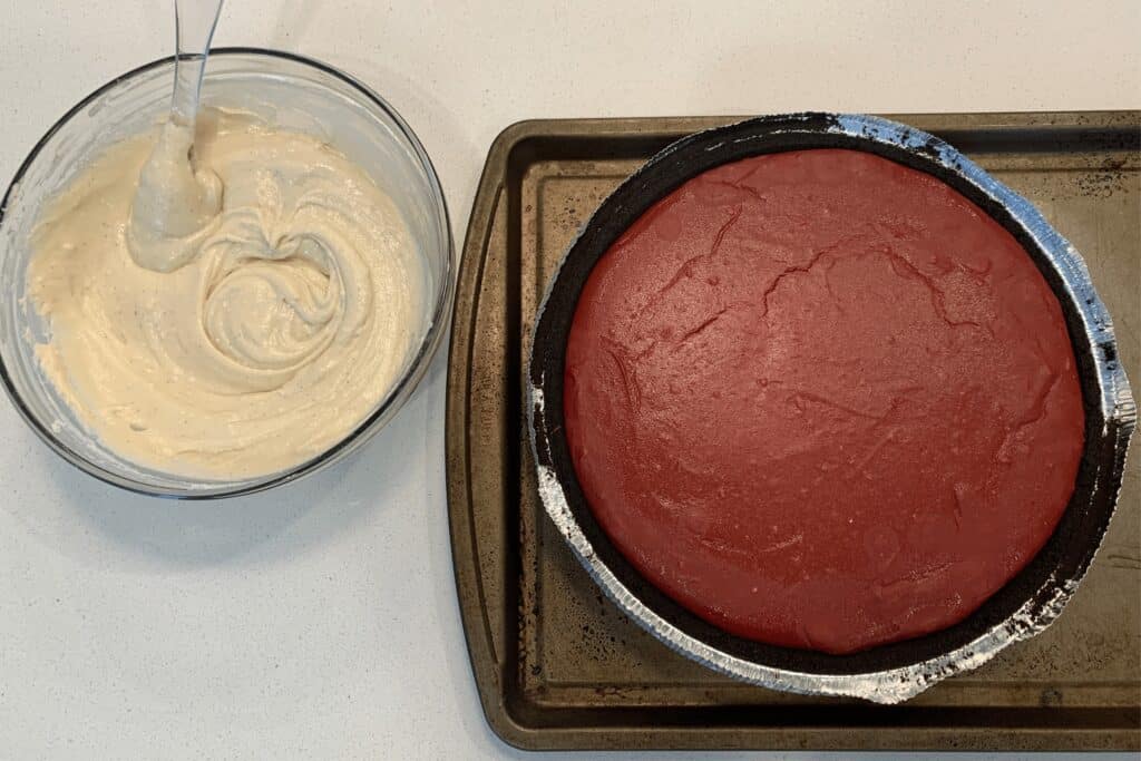 baked red velvet cheesecake beside a bowl of frosting