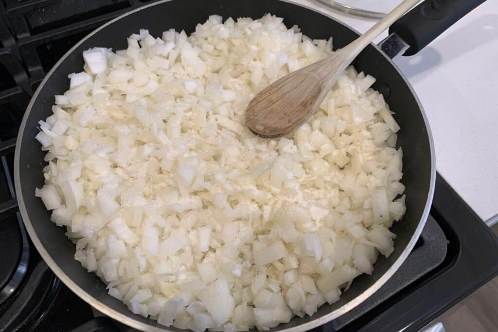 diced onion in a pan with olive oil, salt, and sugar
