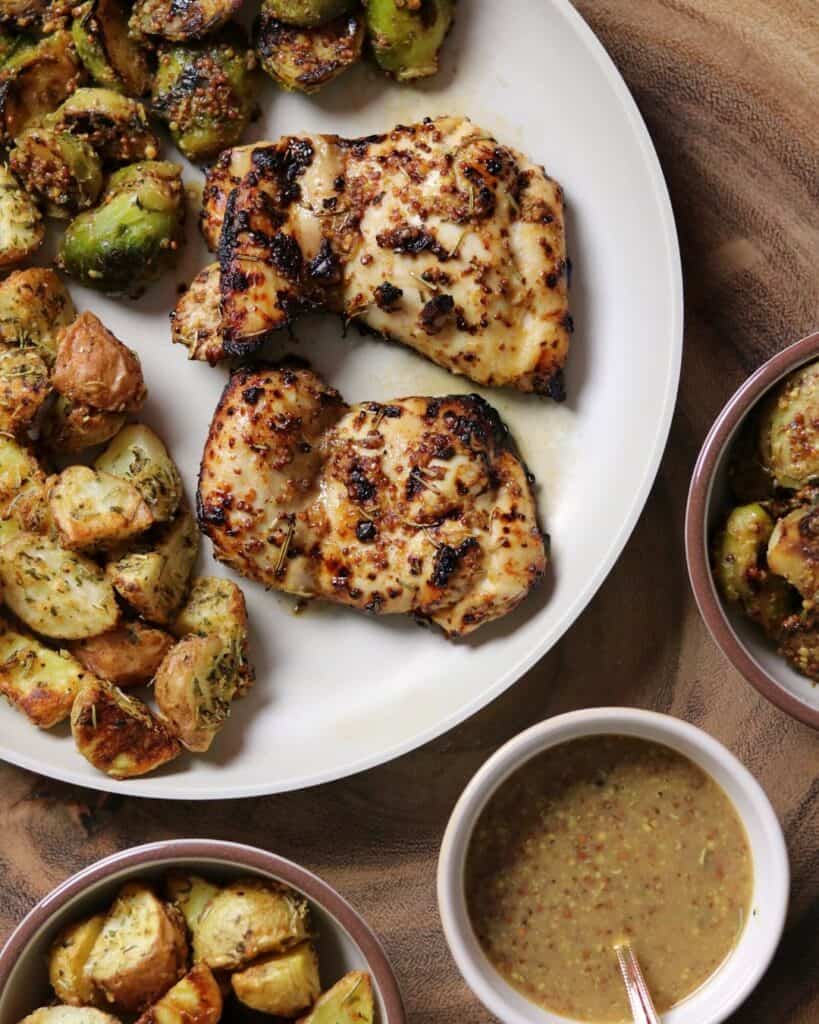 mustard balsamic chicken thighs on a plate with potatoes and brussels sprouts