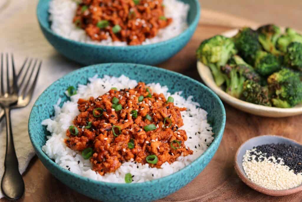 chili coconut ground chicken over rice in a bowl beside air fried broccoli and sesame seeds