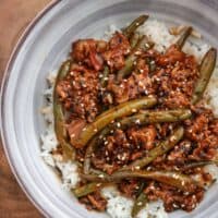 sriracha bbq ground beef in a bowl over rice with toasted sesame seeds and black sesame seeds