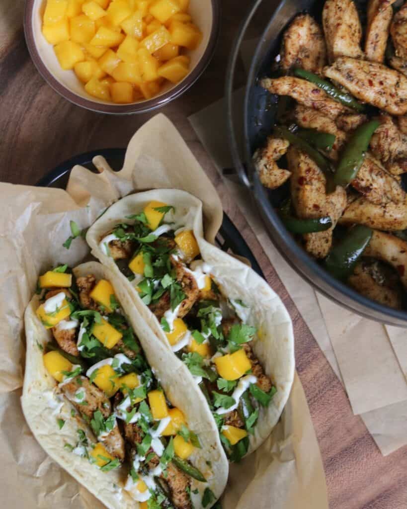 copycat brushfire tacos beside a bowl of diced mango and air fryer basket with jerk chicken and jalapeños