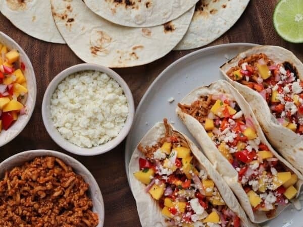 chipotle bbq ground chicken tacos on a plate beside mango salsa and cotija cheese