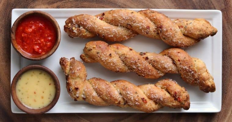 3 bread twists on a white plate with dipping sauce