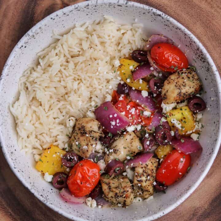 Greek chicken and veggies in a bowl with rice, kalamata olives, feta cheese, and parsley