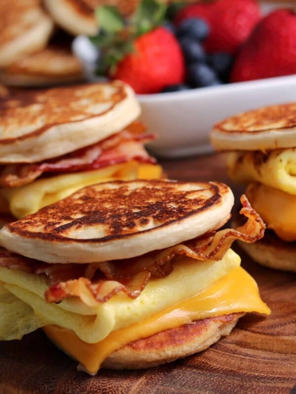 three bacon egg and cheese homemade McGriddles on a cutting board with a bowl of fruit