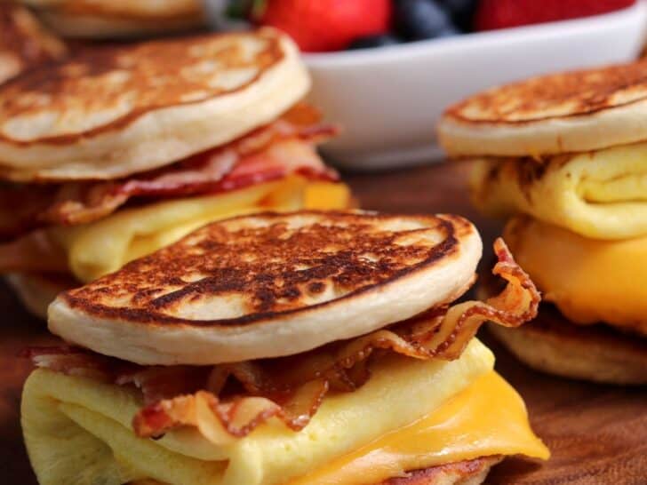 three bacon egg and cheese homemade McGriddles on a cutting board with a bowl of fruit