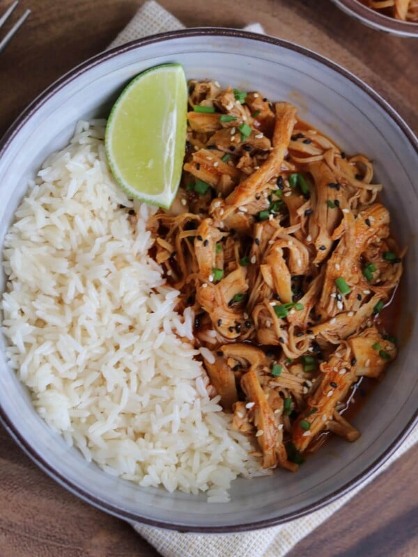 spicy coconut pulled chicken thighs in a bowl with jasmine rice and a lime wedge