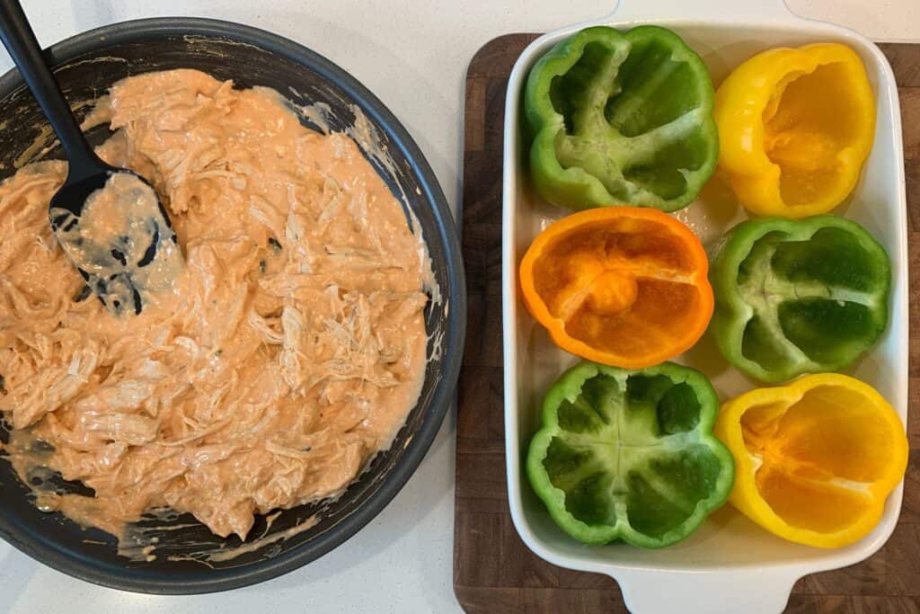 buffalo chicken filling in a skillet with bell peppers in a baking dish