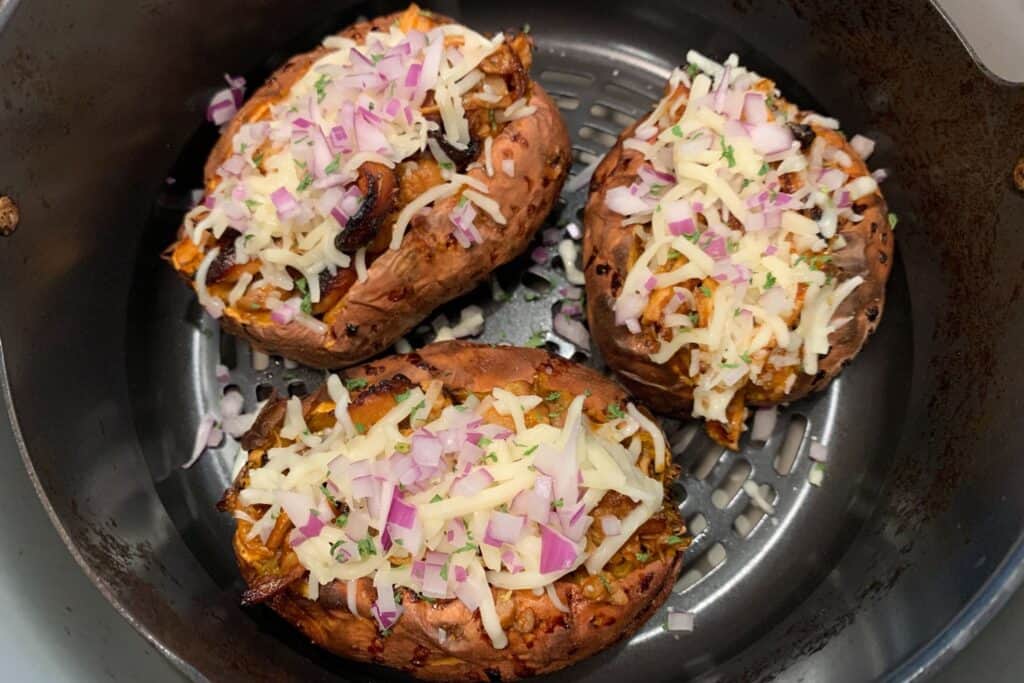 bbq chicken stuffed sweet potatoes in the air fryer basket topped with mozzarella, red onion, and parsley