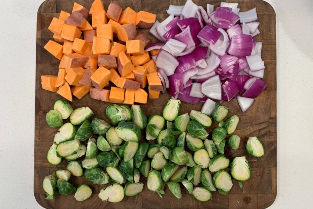 brussels sprouts, sweet potatoes, and red onion on a cutting board