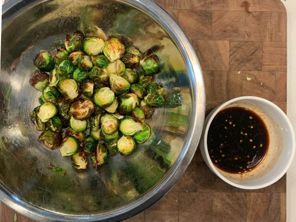 air fried brussels sprouts in a mixing bowl beside a bowl of soy glaze