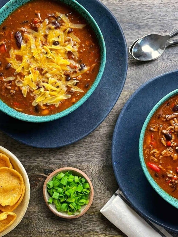 two bowls of turkey chili with corn chips, scallions, and shredded cheese