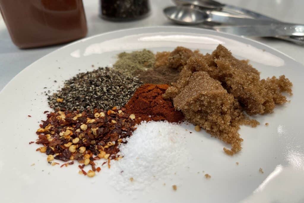 red pepper flakes, salt, pepper, brown sugar, smoked paprika, sage, and allspice on a plate