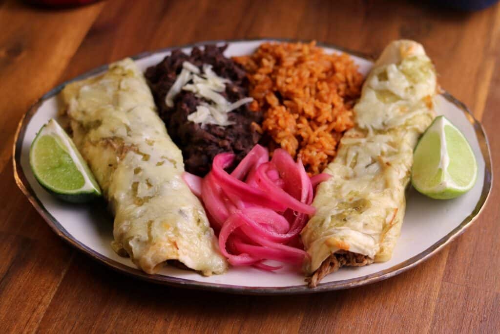 two barbacoa beef enchiladas with refried black beans, spanish rice, and pickled red onion