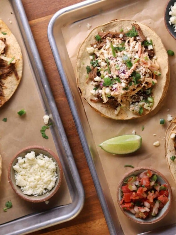 four beef tostadas with slaw on quarter sheet pans with queso fresco, pico, and lime wedges