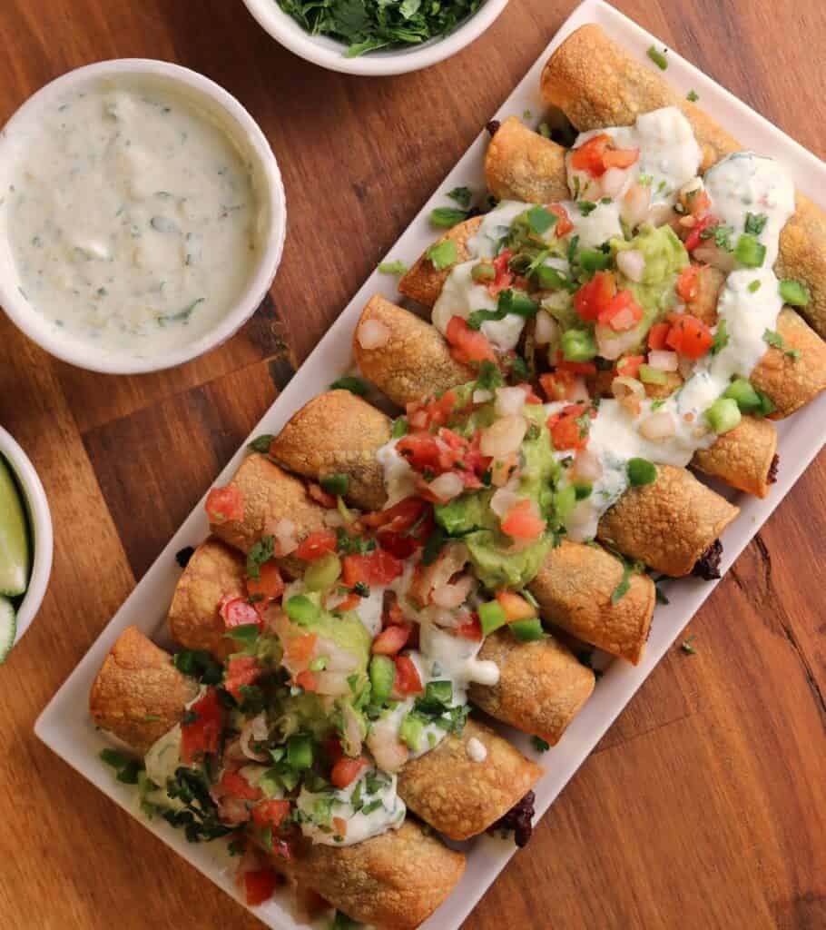 a plate of baked taquitos topped with guacamole, Greek yogurt, and pico de gallo 