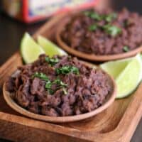 a bowl of refried black beans on a wooden serving plate with lime wedges