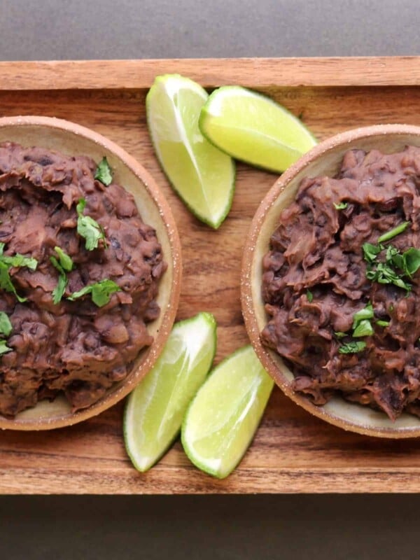 two bowls of refried black beans with lime wedges and cilantro